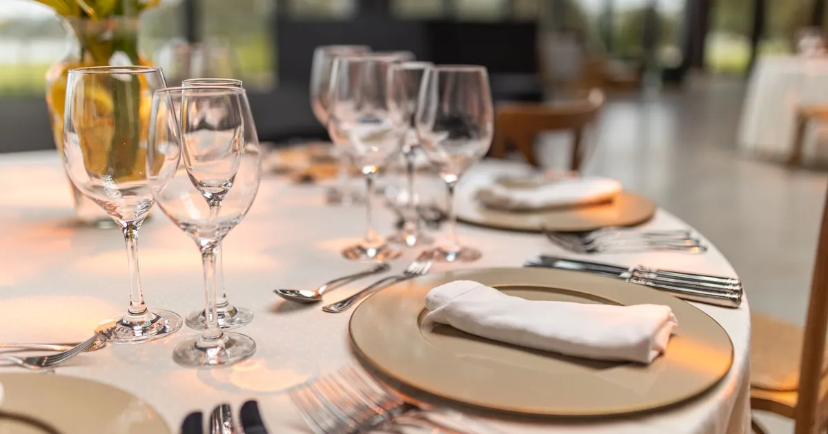 A dining table set with wine glasses, white napkins and gold charger plates
