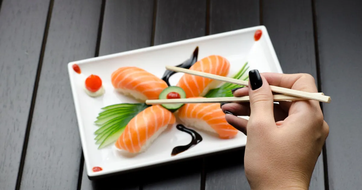 Salmon nigiri on a white plate, picked up with chopsticks